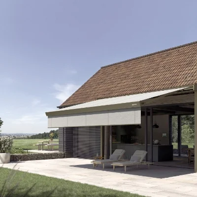 Markise am Haus, die einen Schatten auf die Terrasse mit zwei Liegestühlen wirft.